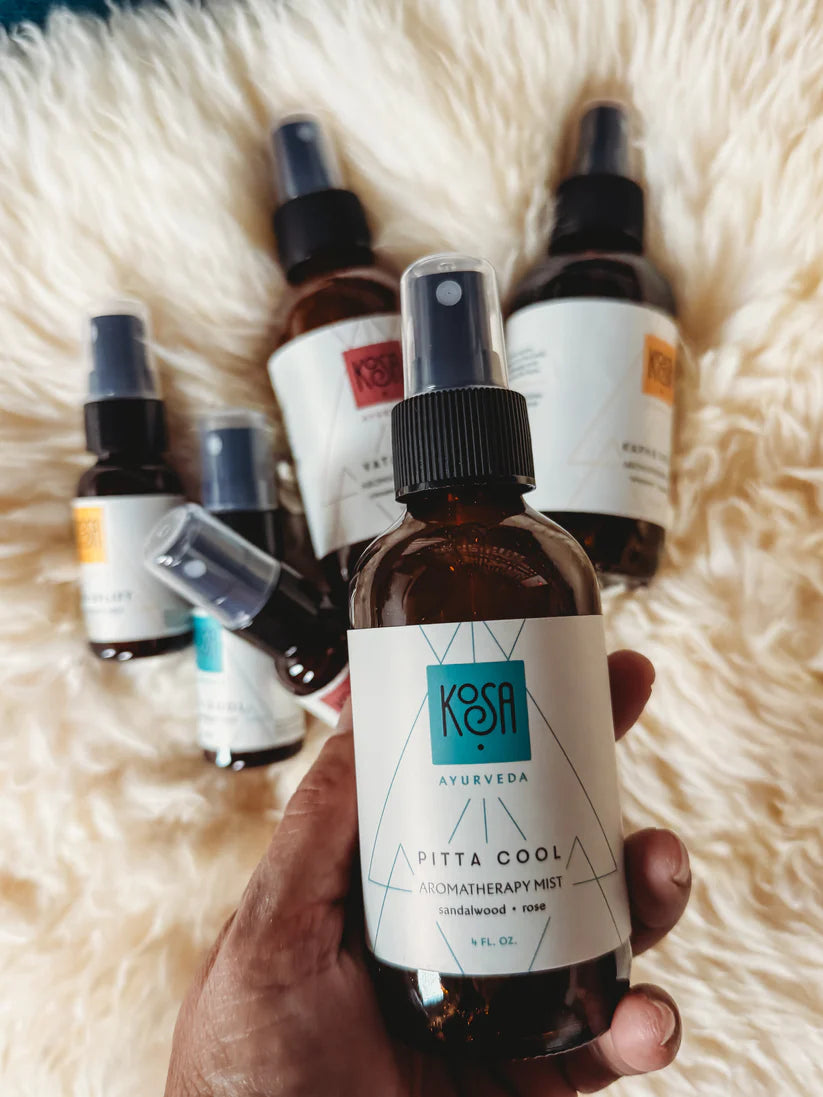 Hand holding a bottle of Kosa Ayurveda Pitta Cool Ayurvedic mist on a fluffy white surface.